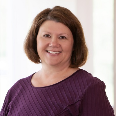 Woman with short brown hair and a purple top, smiling at the camera