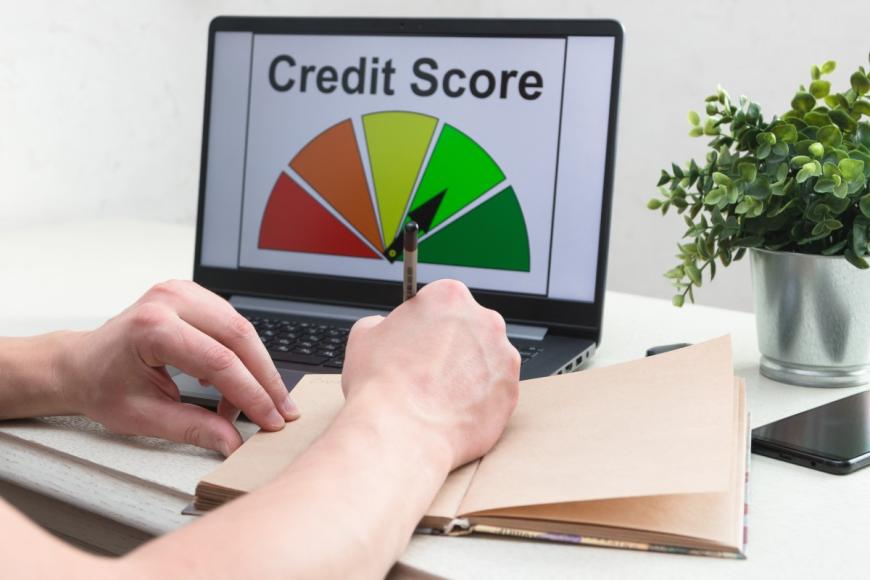 Person writing in notebook. Graphic of Credit Score on laptop screen