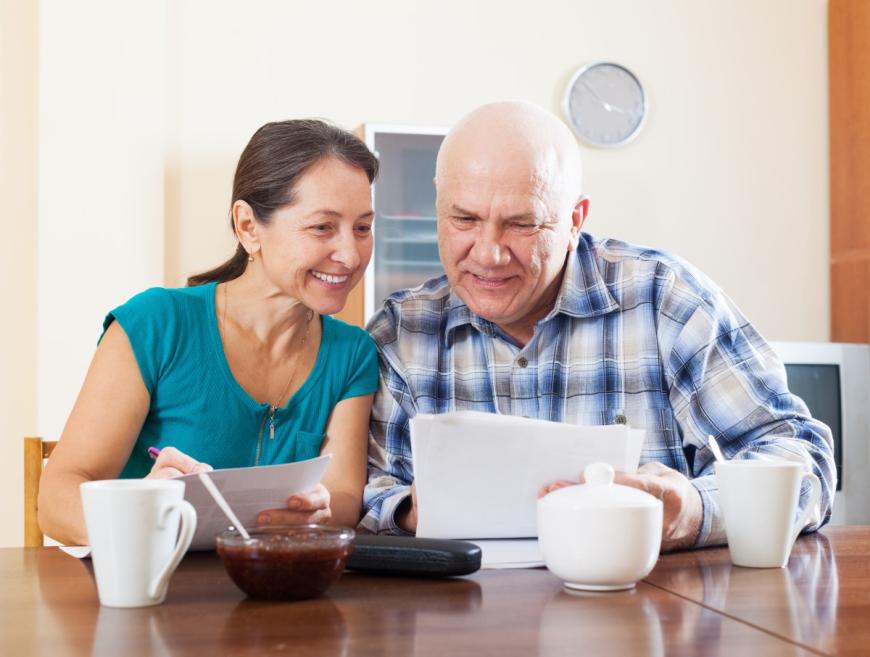 Older man and woman looking over paper smiling and holding coffee cups