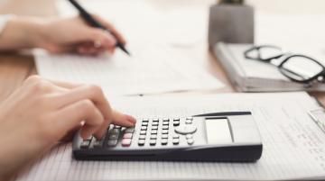 Hands of an individual using a calculator and writing notes