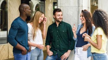 Multiracial group of adults standing outside next to a building, smiling and enjoying each other