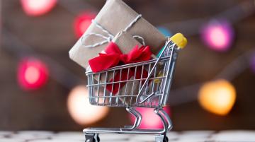 Metal shopping cart with two wrapped presents in its basket.  Behind the cart are blurry images of multi-colored lights.